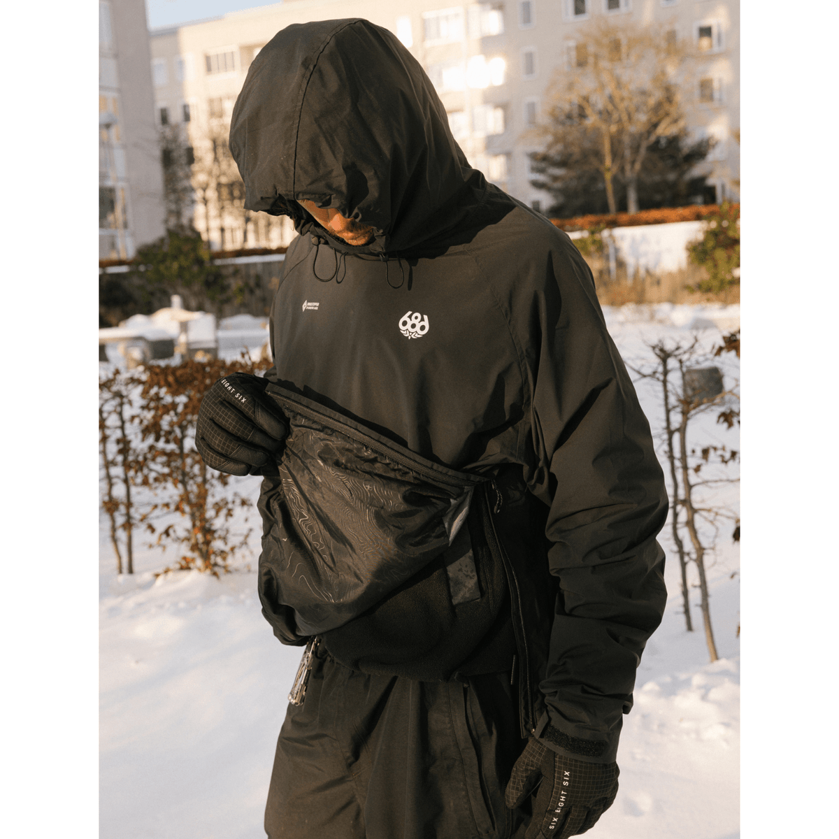 686 men's hooded pullover windbreaker with fanny pack worn outdoors in snow