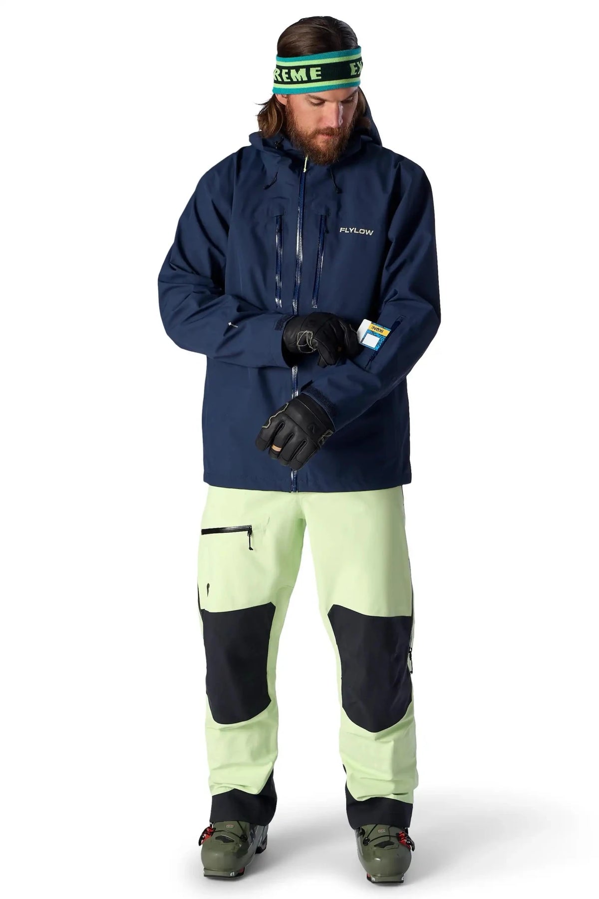 Flylow men's ski jacket in navy blue shown with light green ski pants on male model