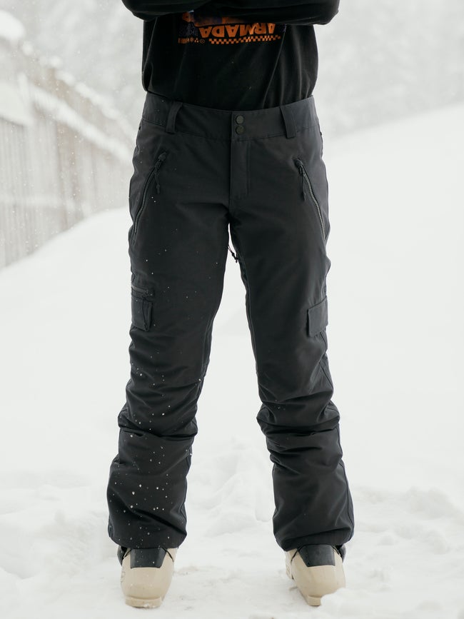 Women's insulated ski pants with cargo pockets and zippered details, worn in snowy setting.