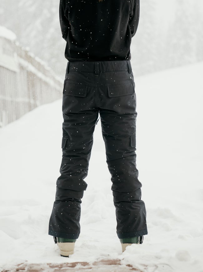 Women's insulated snow pants with cargo pockets shown from the back in snowy conditions.