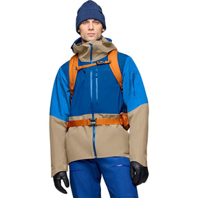 Men's two-tone ski jacket with large hood, worn with orange backpack and blue pants.