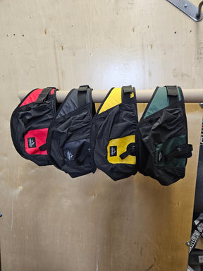 Four Larrabee Gearworks Parawing Stash Belt V2 harnesses in red, black, yellow, and green hanging on a rod