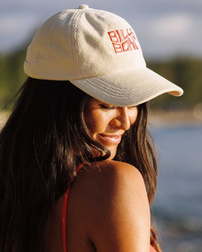 Billabong cream corduroy dad cap with red embroidered logo worn outdoors