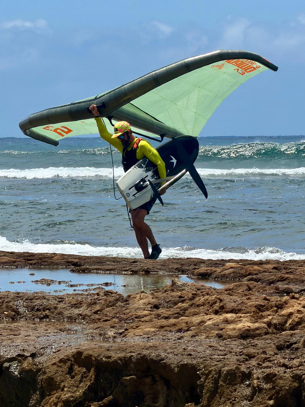 Five-O Dynamo V3 wing in green and black held by rider at rocky ocean shoreline