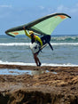 Five-O Dynamo V3 wing in green and black held by rider at rocky ocean shoreline