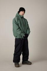 Men's shell ski jacket in muted green with hood, worn with black snow pants and gloves