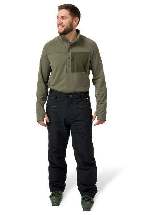 Men's technical ski pants with multiple zip pockets worn with ski boots, full length view.