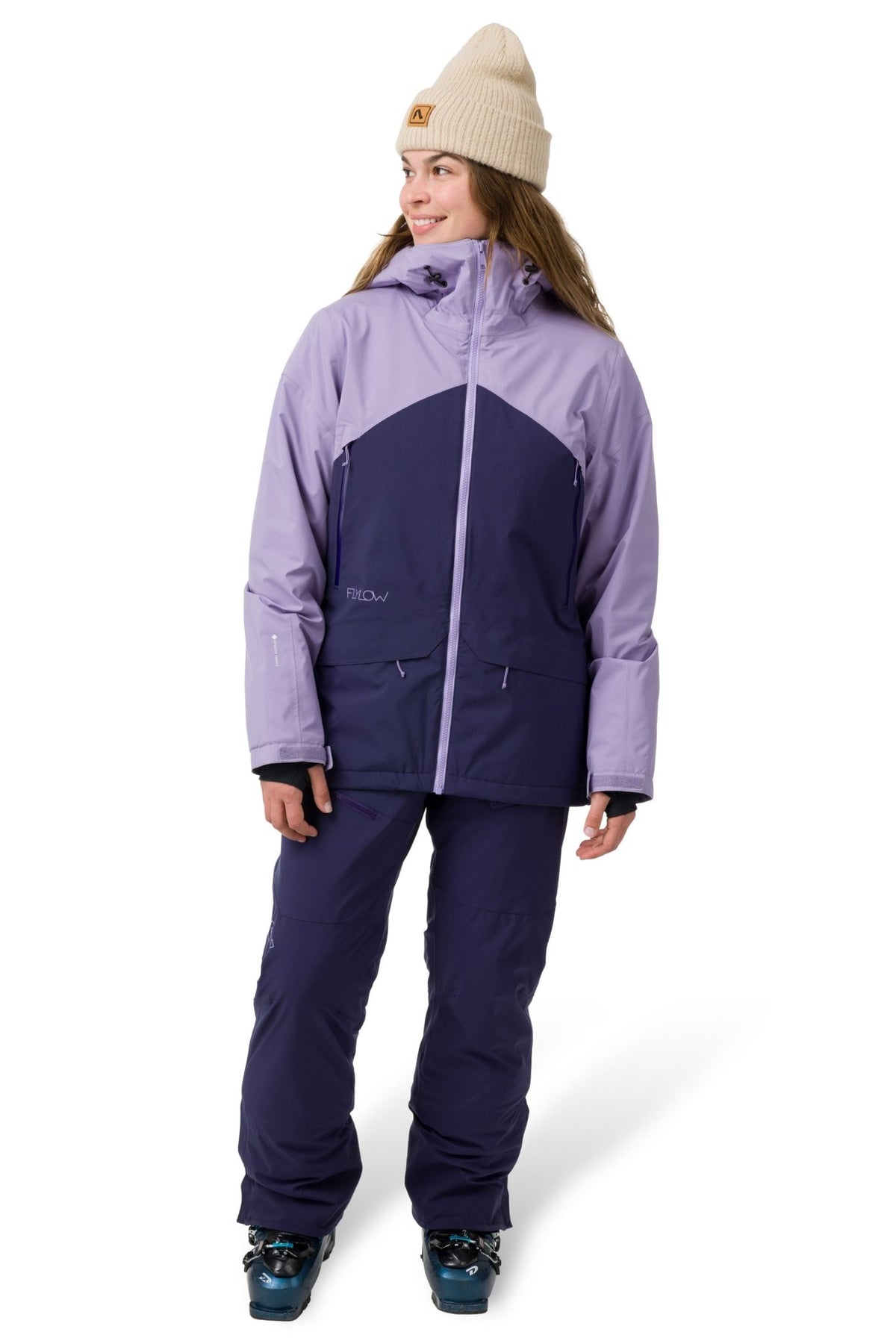 Women's two-tone ski jacket with hood, worn with matching snow pants and ski boots