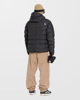 Volcom men's quilted puffer jacket with hood, shown from rear on model with snow pants and Vans sneakers.
