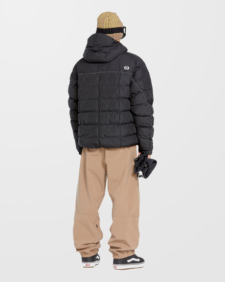 Volcom men's quilted puffer jacket with hood, shown from rear on model with snow pants and Vans sneakers.