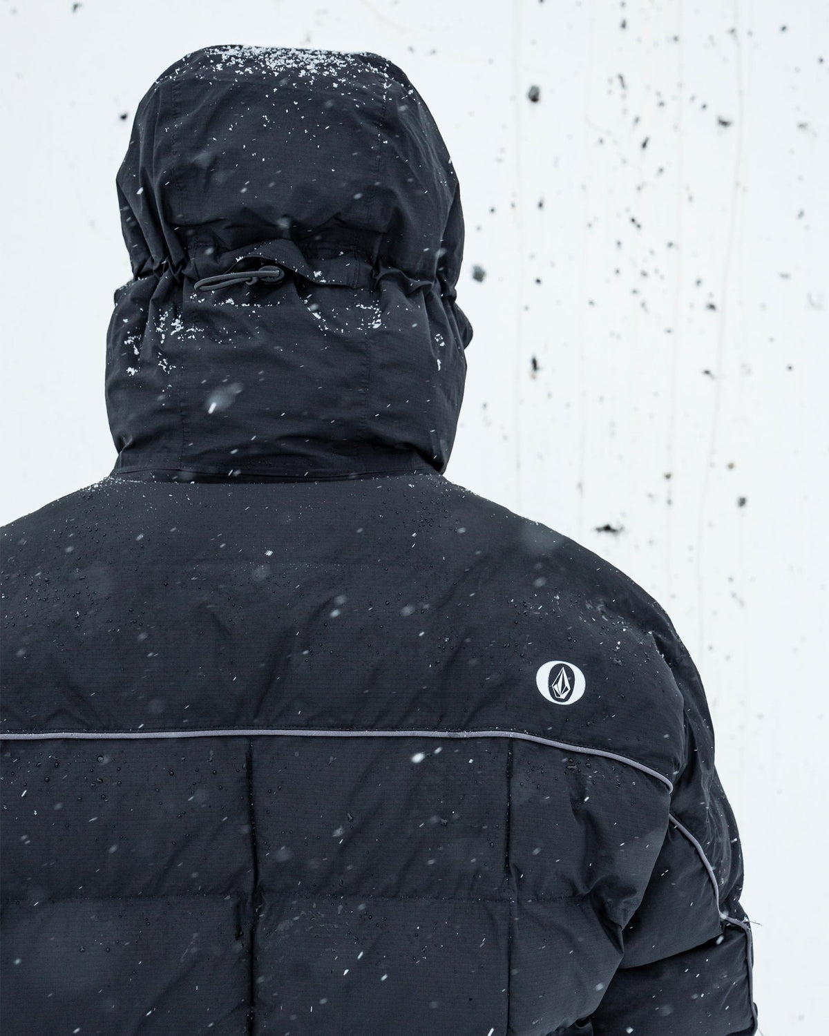 Volcom men's insulated hooded jacket with reflective piping detail, shown from back in snowy conditions.