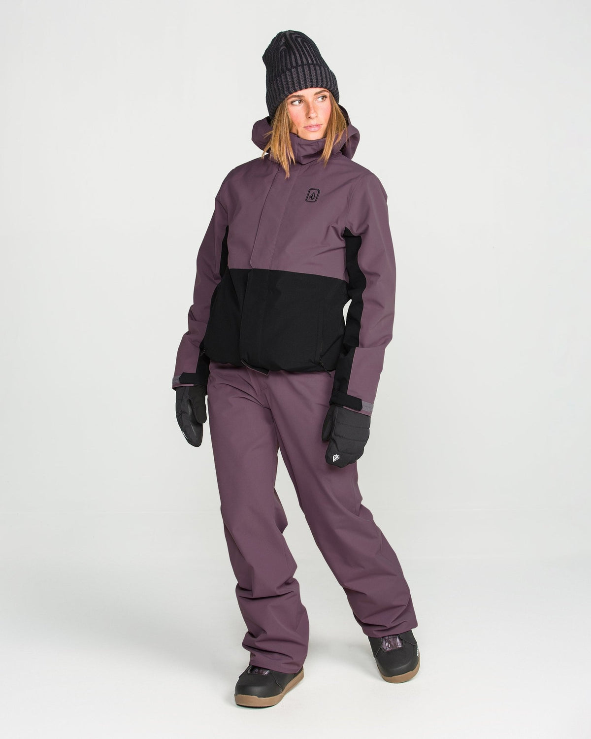 Women's insulated two-tone snowboard jacket with hood, worn with matching pants and gloves.