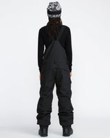 Women's snow bib pants with crossback straps, cargo pockets, and relaxed fit, shown from behind.