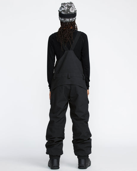 Women's snow bib pants with crossback straps, cargo pockets, and relaxed fit, shown from behind.