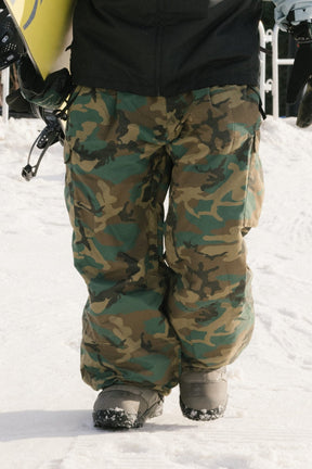 686 men's camo print cargo snow pants with snowboard boots on snowy slope