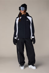 Women's shell ski jacket with hood, worn with matching black snow pants and goggles