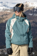 686 women's shell ski jacket with colorblock paneling worn by smiling model on snowy mountain