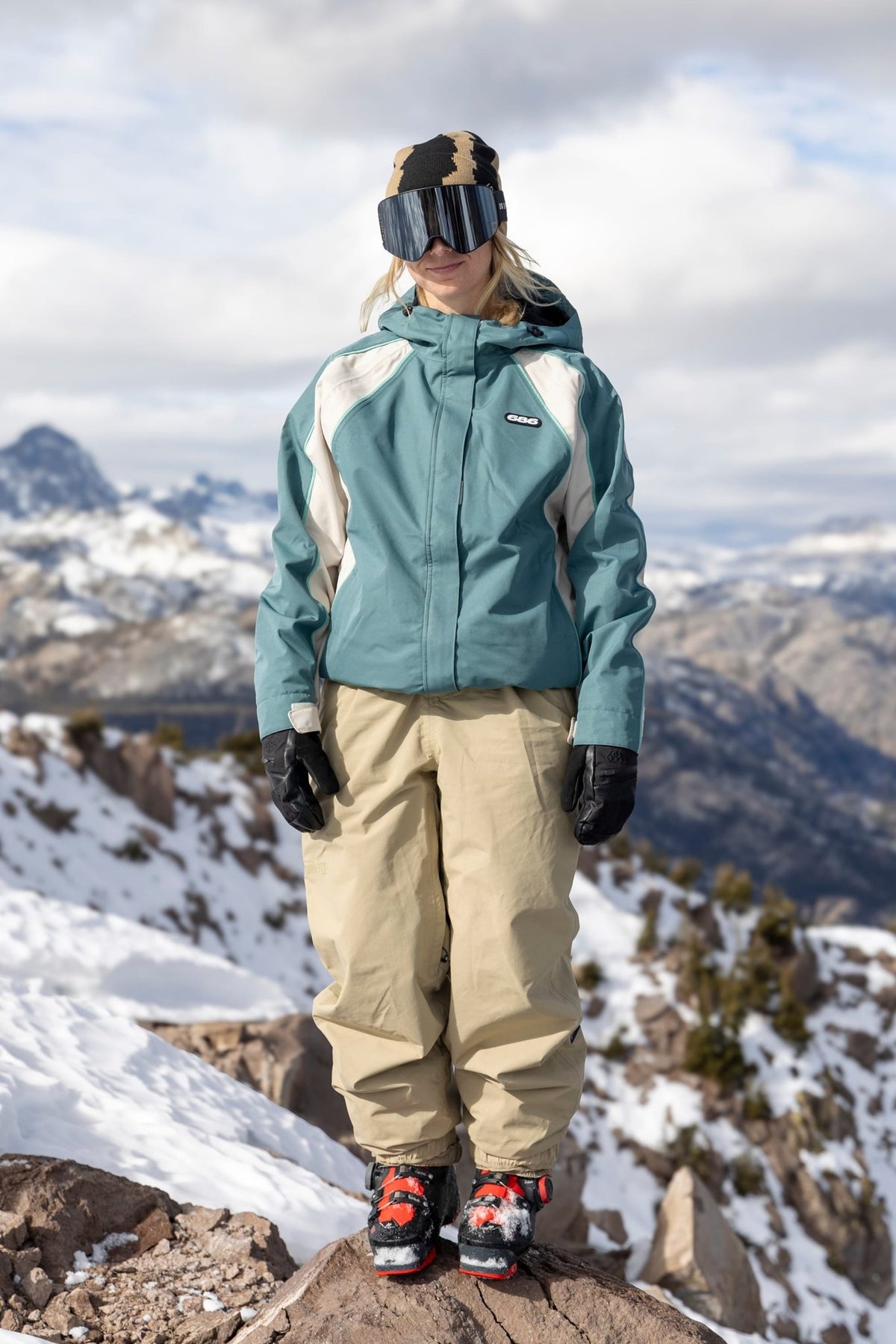 Women's shell ski jacket with colorblock panels worn on snowy mountain summit