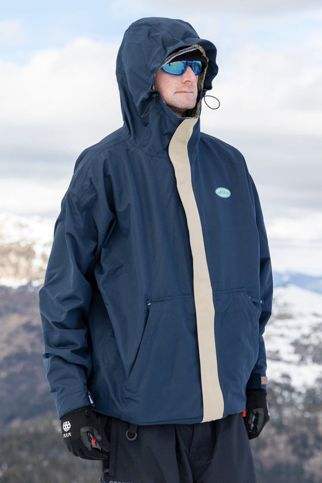 Men's hooded snow jacket with colorblock front panel, worn on a snowy mountain.