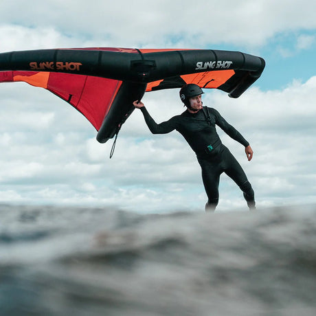 Man windsurfing on water with red and black Slingshot wing, wearing wetsuit and helmet