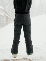 Women's insulated snow pants with cargo pockets shown from the back in snowy conditions.