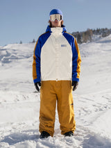 Men's insulated snow pants in a warm golden hue, worn with matching ski jacket on snowy slope.