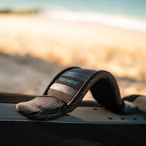 Black foot strap for board sports on a board with sand and ocean in the background