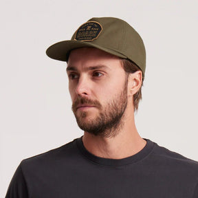 Olive green Roark snapback cap with black embroidered patch logo on male model