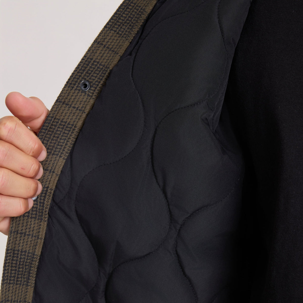 Close-up interior view of women's plaid jacket showing quilted black lining and snap closure