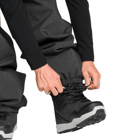 Men's snow pants with integrated gaiter being fitted over winter snowboard boot