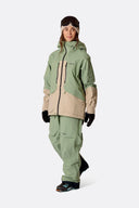 Women's Rab Bigline ski jacket with two-tone design, worn with matching green pants and ski boots.